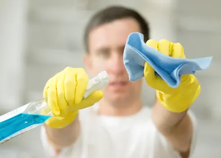 Person mit Schutzhandschuhen, Reinigungstuch und Sprühflasche